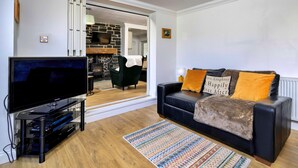 Ein modernes Wohnzimmer mit Flachbildfernseher, einer Couch mit Zierkissen, einem gemusterten Teppich und einem Kamin aus Stein.