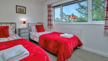 A bedroom with two beds, a nightstand, a lamp, a window with a view of trees, and a radiator.