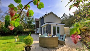 Eine Terrasse mit Gartenmöbeln, einem Blumentopf und Blick auf ein Haus mit Satteldach.