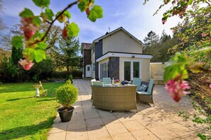 A patio area with outdoor furniture, a potted plant, and a view of a house with a sloped roof. - Luxury Country Estate Near Largs (Betws-Y-Coed)