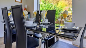 Ein Esszimmer mit Tisch, Stühlen, Tellern, Besteck und Gläsern, mit Blick auf grüne Vegetation.