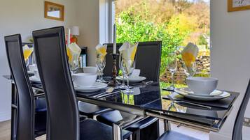 A dining table set with chairs, plates, cutlery, and glasses, with a view of greenery outside.
