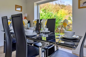 A dining table set with chairs, plates, cutlery, and glasses, with a view of greenery outside. - Luxury Country Estate Near Largs (Betws-Y-Coed)