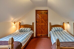 A bedroom with two wooden beds, a slanted ceiling, and a wooden door. - Luxury Whitby Townhouse for 10 (Bude)