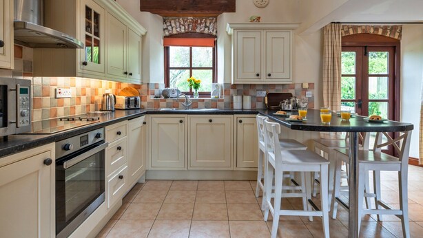 A kitchen with a central island, white cabinetry, and a window with a view of greenery. - Luxury Whitby Townhouse for 10 (Bude)