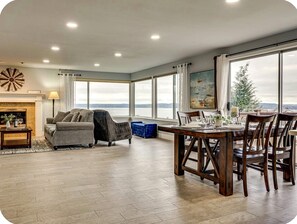 A spacious living room with a fireplace, a dining area with a view, and a large window overlooking a body of water. - Spacious Sound View Top Floor Apartment with Large Deck (Federal Way)