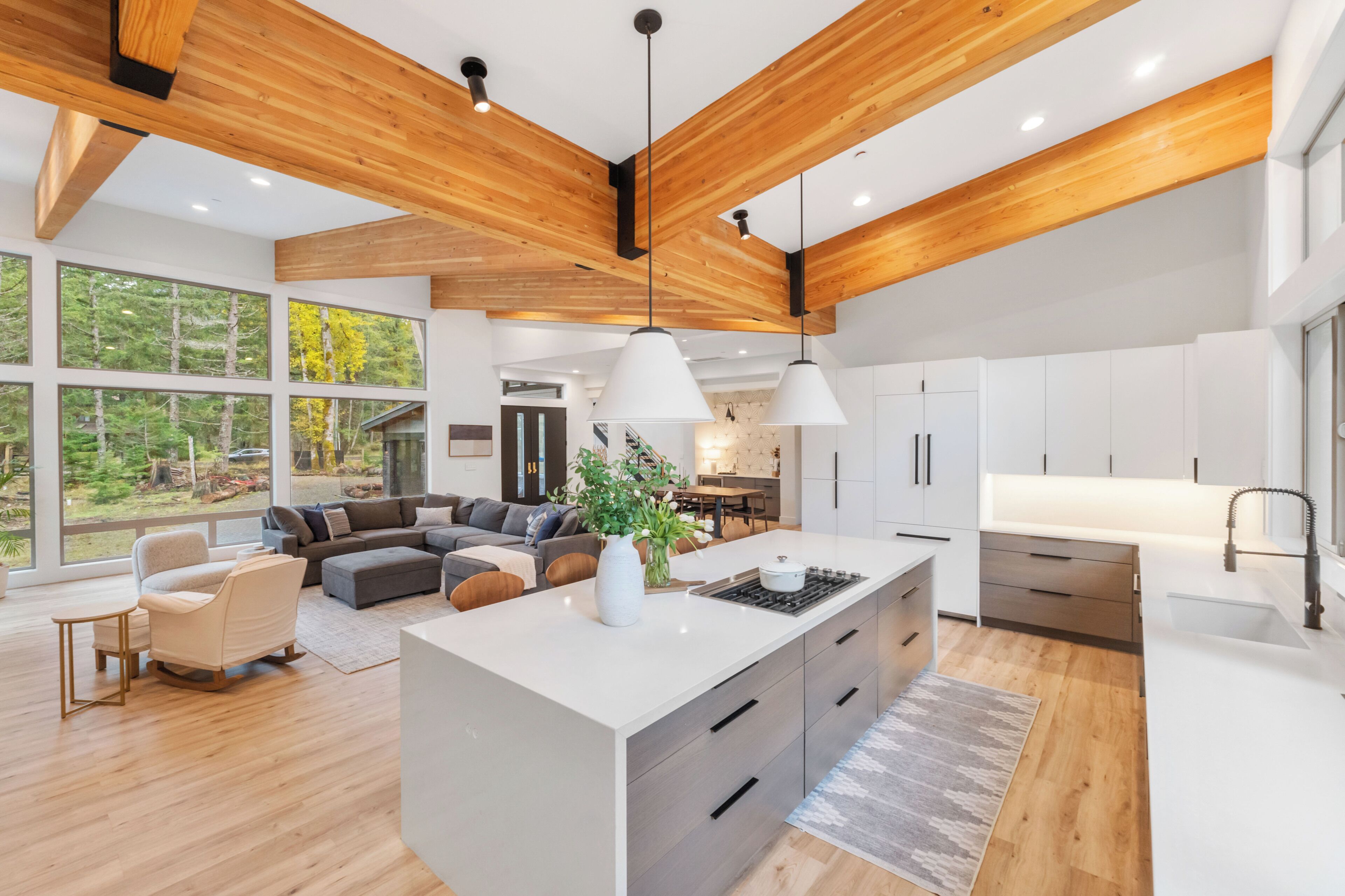 A modern kitchen with a central island, white cabinetry, and a view of a forest through large windows.