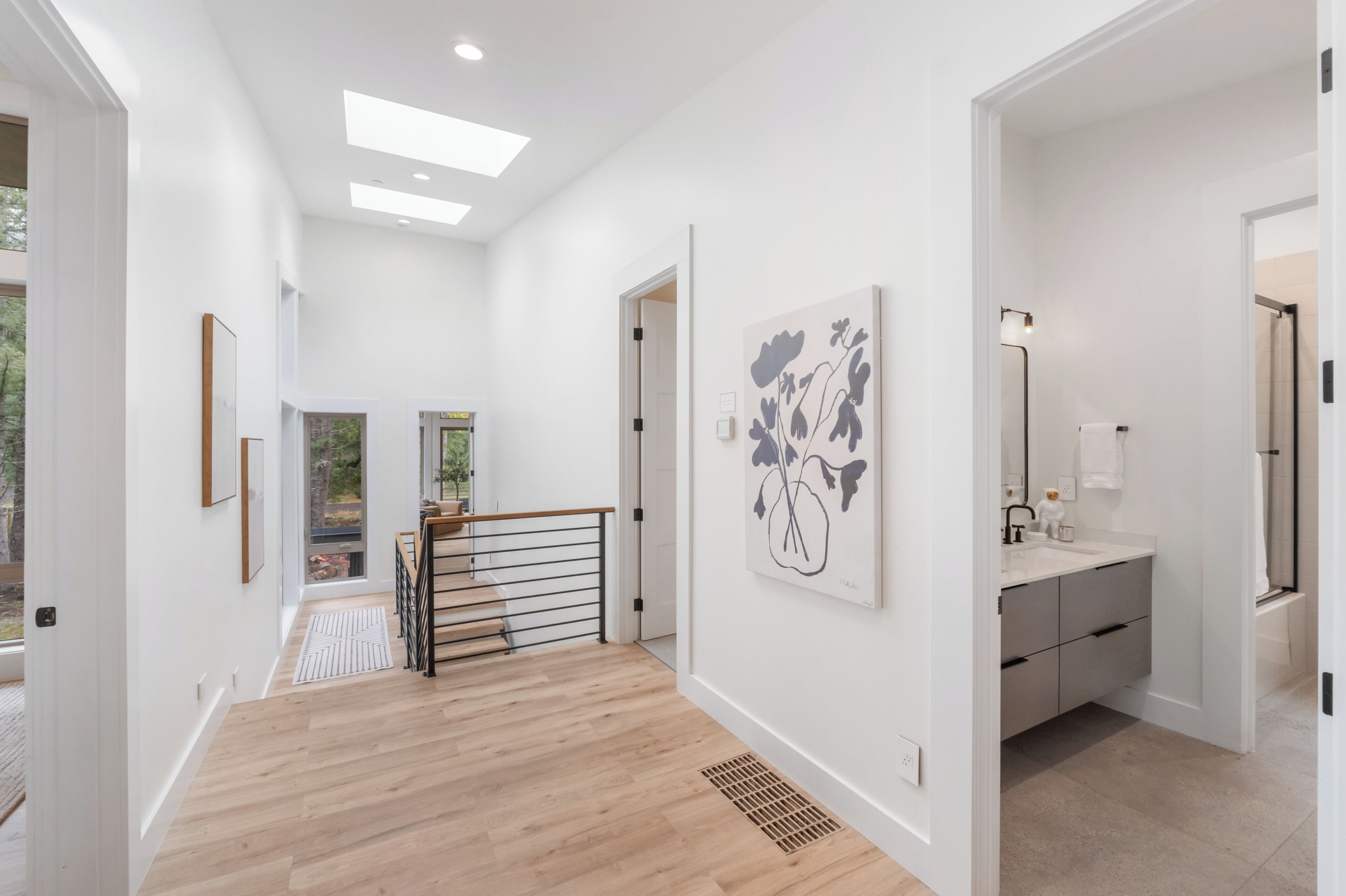 A modern interior with a wooden staircase, a large artwork on the wall, and a bathroom with a mirror and sink.