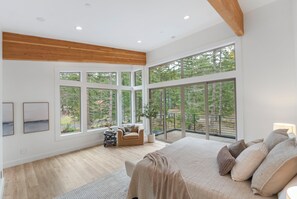 A spacious bedroom with large windows, a bed, a chair, and a small table. - Luxury Mountain Getaway Minutes from Crystal Mountain & Mount Rainier (Enumclaw)
