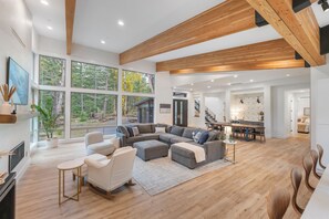 A spacious living area with a large sectional sofa, a fireplace, and a view of the outdoors through large windows. - Luxury Mountain Getaway Minutes from Crystal Mountain & Mount Rainier (Enumclaw)