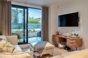 A modern living room with a sofa, a small table, a TV mounted on the wall, and a sliding glass door leading to an outdoor area. - Stylish City Apartment With Terrace (Plymouth)