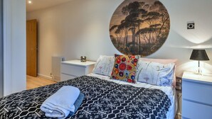 Un dormitorio con cama, mesita de noche, lámpara, radiador y puerta.