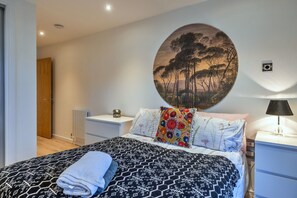 Ein Schlafzimmer mit Bett, Nachttisch, Lampe, Heizkörper und einer Tür.