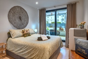 A bedroom with a bed, a large wall tapestry, a view of the outside, and a small table with a vase. - Stylish City Apartment With Terrace (Plymouth)