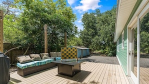 Terraza al aire libre con sofá modular y una mesa, rodeada de árboles y un edificio.