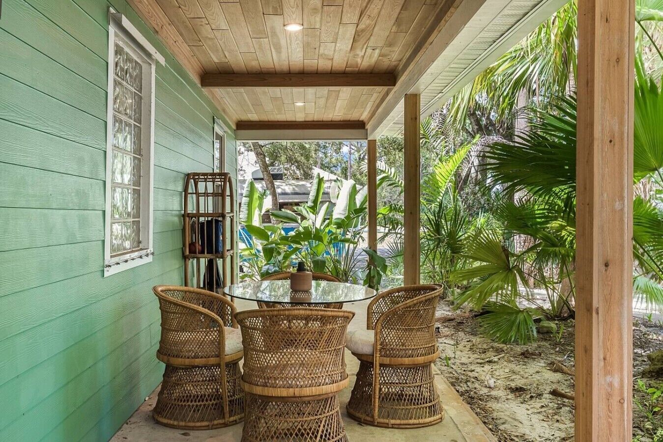 A covered patio with a table and chairs, surrounded by greenery.
