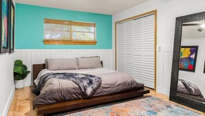 Un dormitorio con cama, ventilador de techo, ventana con persianas, armario y espejo.