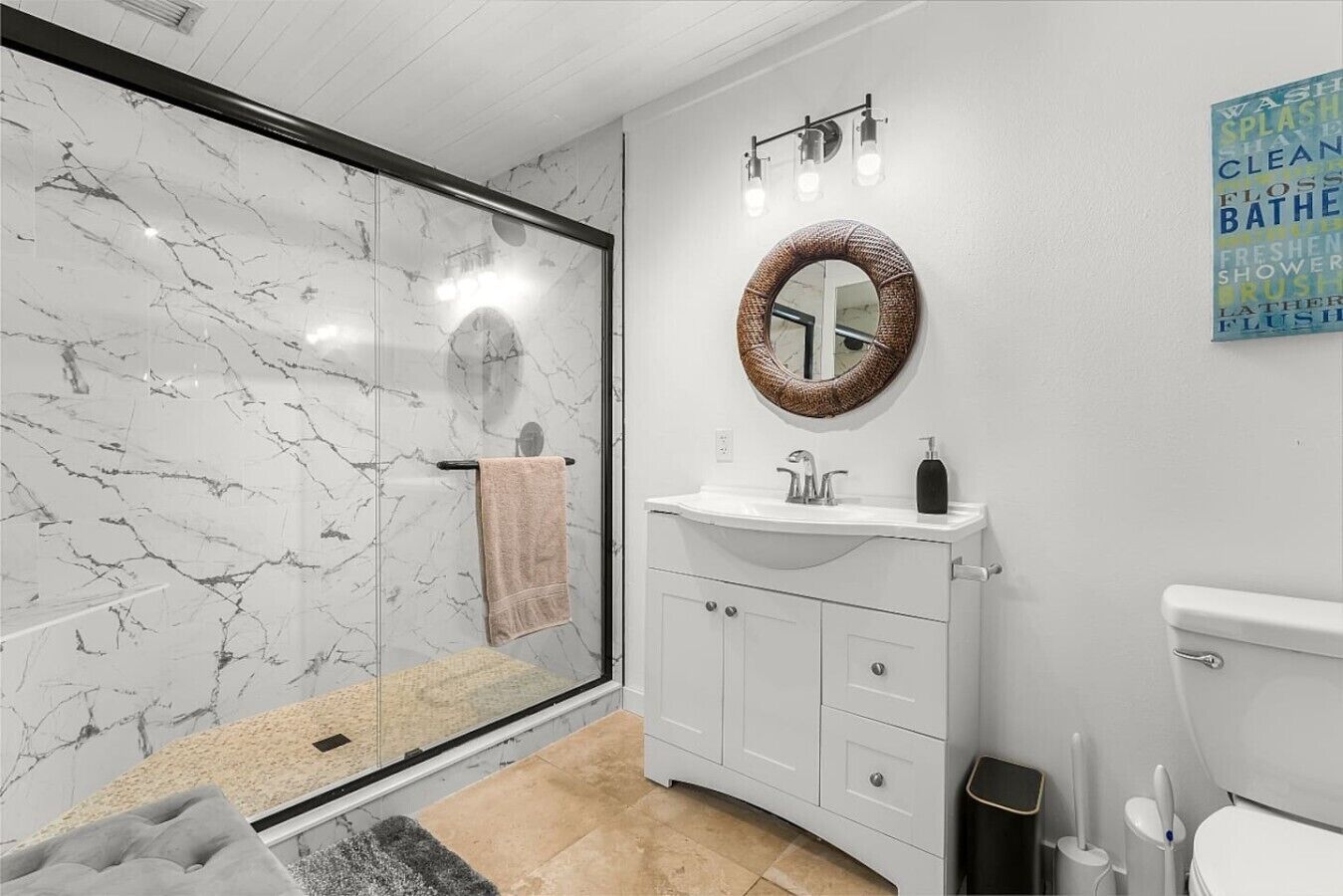 Un baño con cabina de ducha de vidrio, un espejo redondo, un lavamanos blanco y un inodoro.