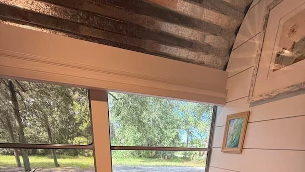 Una habitación con escritorio de madera y una silla, una ventana con vistas a un parque, y un cuadro colgado en la pared.