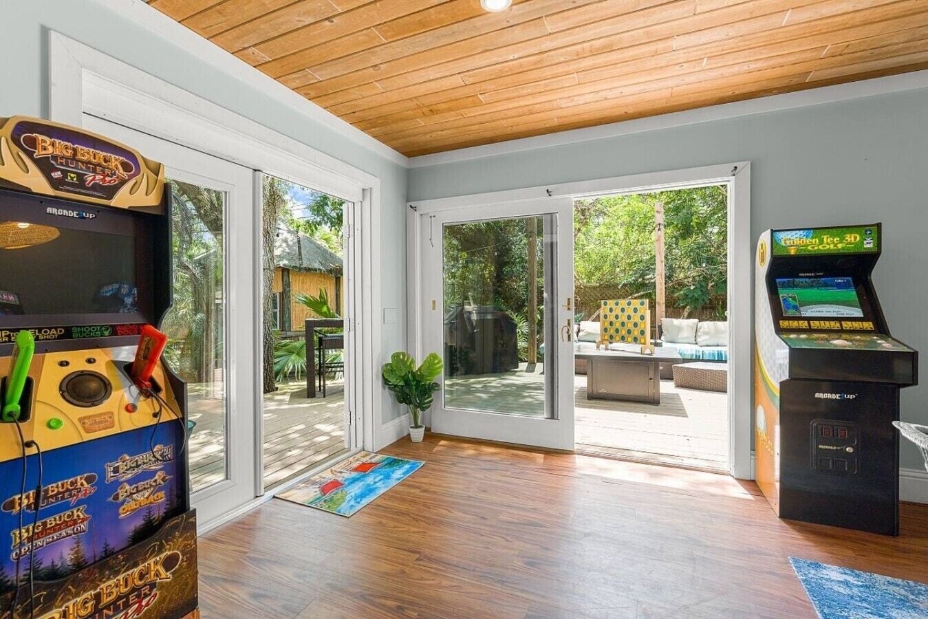 Una stanza con soffitto in legno, un'ampia porta scorrevole in vetro che dà su uno spazio esterno e due cabinati arcade.