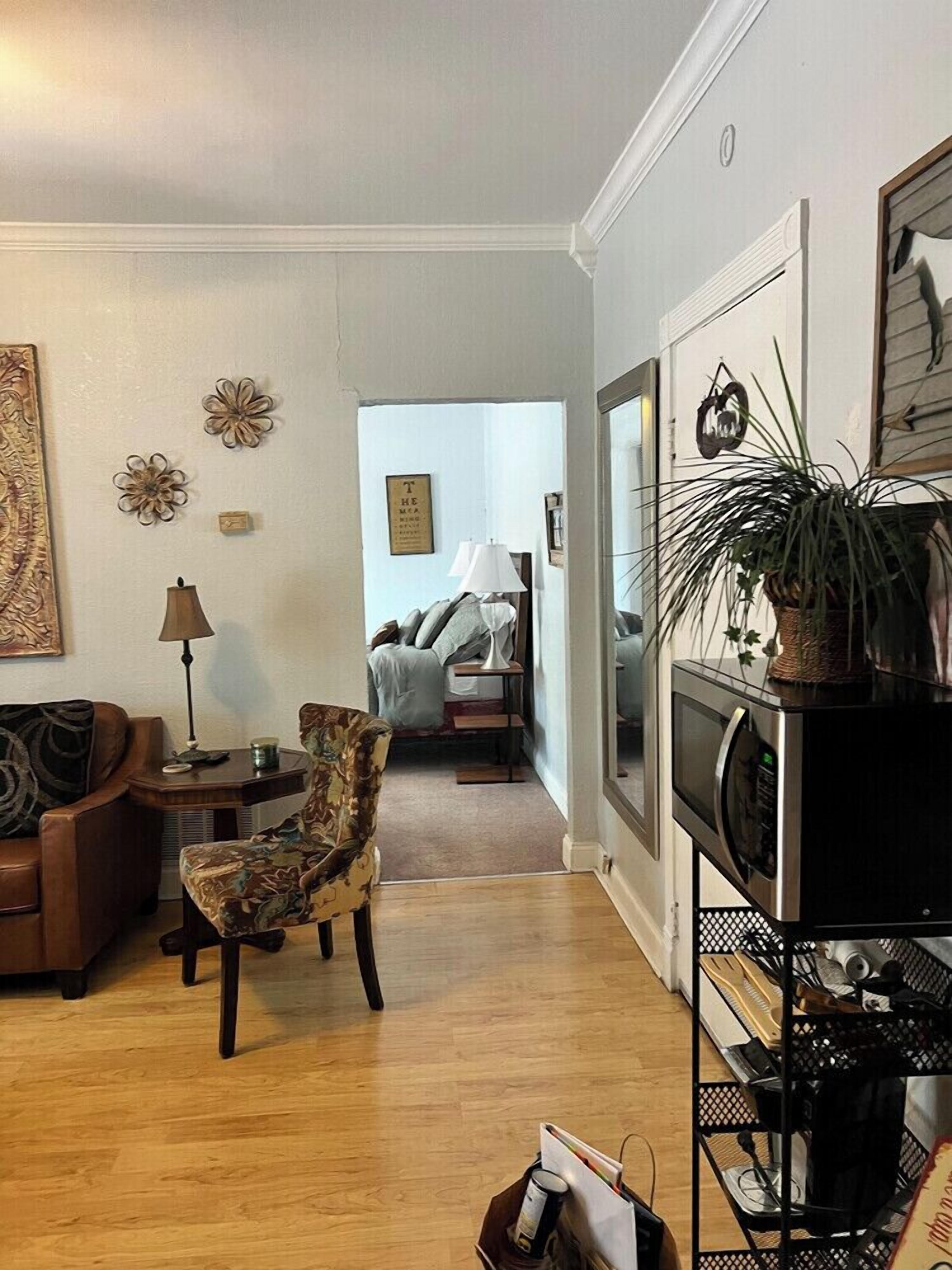 A living room with a sofa, armchair, and a coffee table. There is a television on a stand and a plant on a shelf.