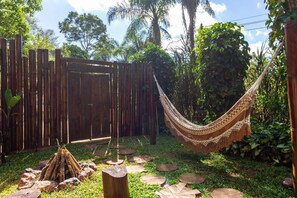 A hammock in a garden with a wooden fence and a fire pit.