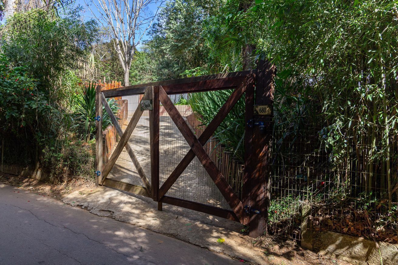 A gated entrance with a wooden gate and metal mesh, surrounded by dense foliage.