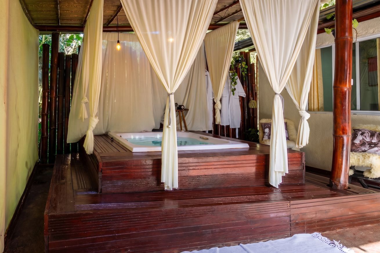 Uma área de spa com hidromassagem, piso de madeira e cortinas brancas.