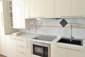 A kitchen with white cabinets, a black sink, a built-in oven, and a countertop with a glass container. - In the heart of 19th-century Rome, a spacious apartment for families and groups (Roma)