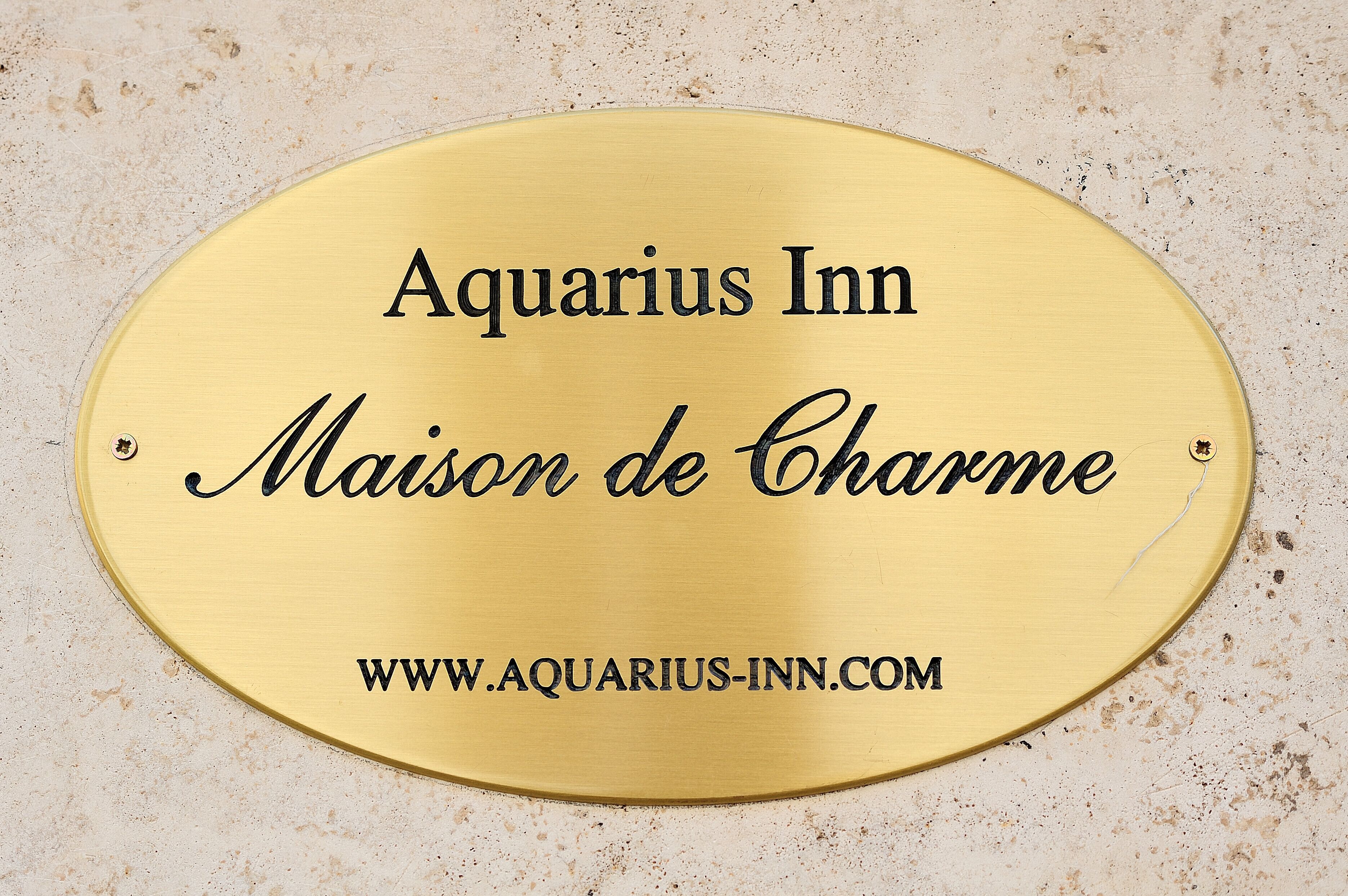 Eine Messingschild mit dem Text 'Aquarius Inn Maison de Charme' und der Webseite 'WWW.AQUARIUS-INN.COM'.