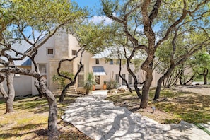A pathway leading to a building with stone walls and multiple windows, surrounded by trees. - Light-filled oasis in the Texas Hill Country (San Antonio)