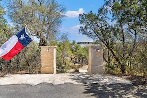 A flag at the entrance of a building with stone pillars and a paved path leading to it. - Light-filled oasis in the Texas Hill Country (San Antonio)