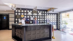 Een receptiebalie met een zwarte toonbank, meerdere klokken en een bord dat het receptiegebied aangeeft.