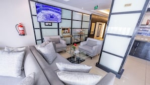 Een moderne hotellobby met een ruime bank, een glazen salontafel en een flatscreen aan de muur.