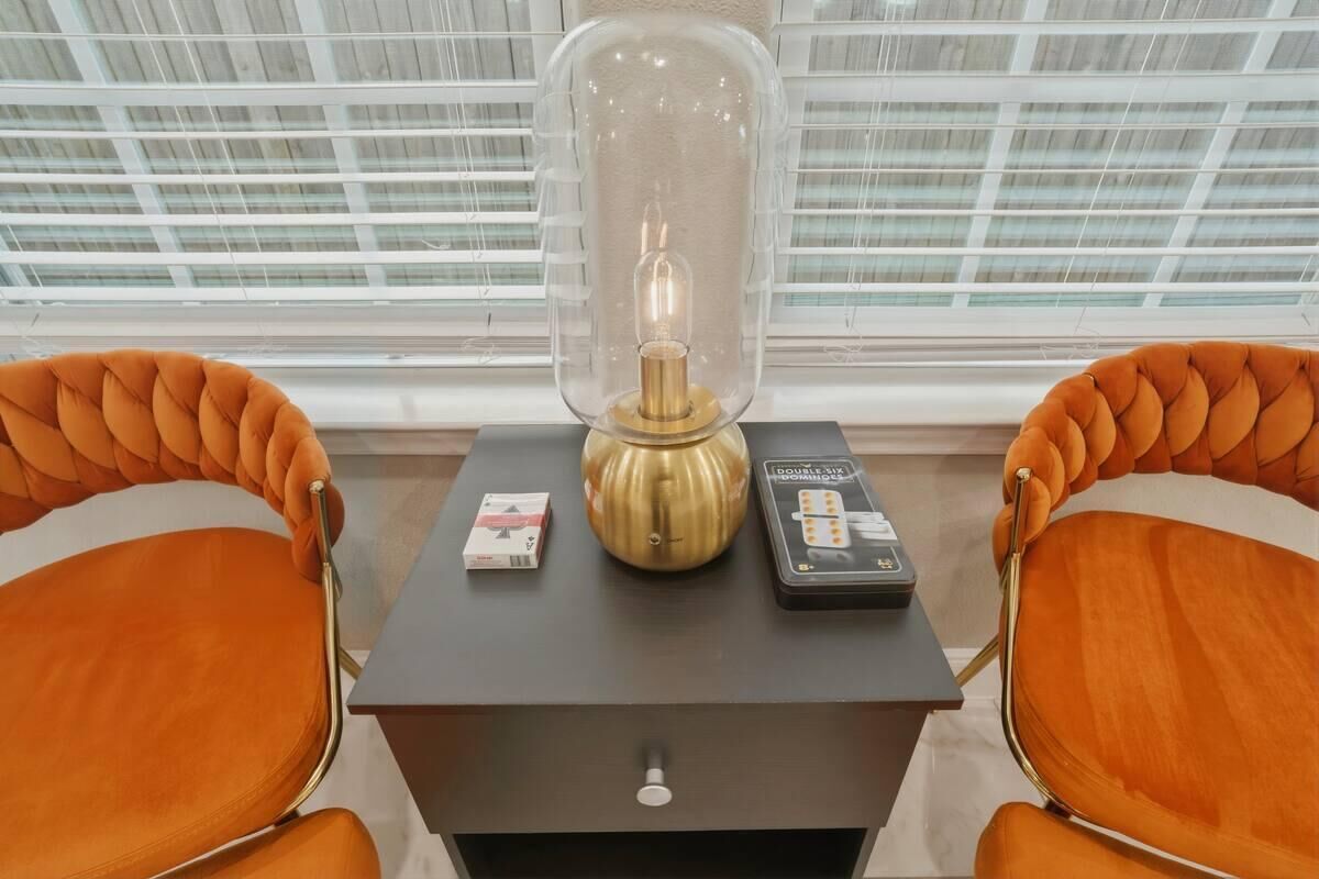 Ein Zimmer mit zwei orangefarbenen Polstersesseln, einem Tisch mit Lampe, einer Kiste und einer Blisterpackung Medikamente.