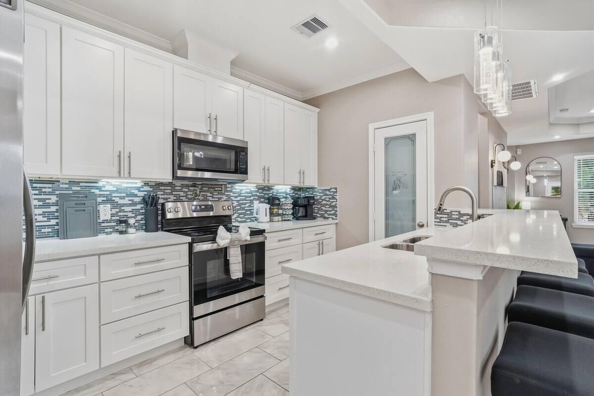 A modern kitchen with white cabinetry, a built-in microwave, and a tiled backsplash.