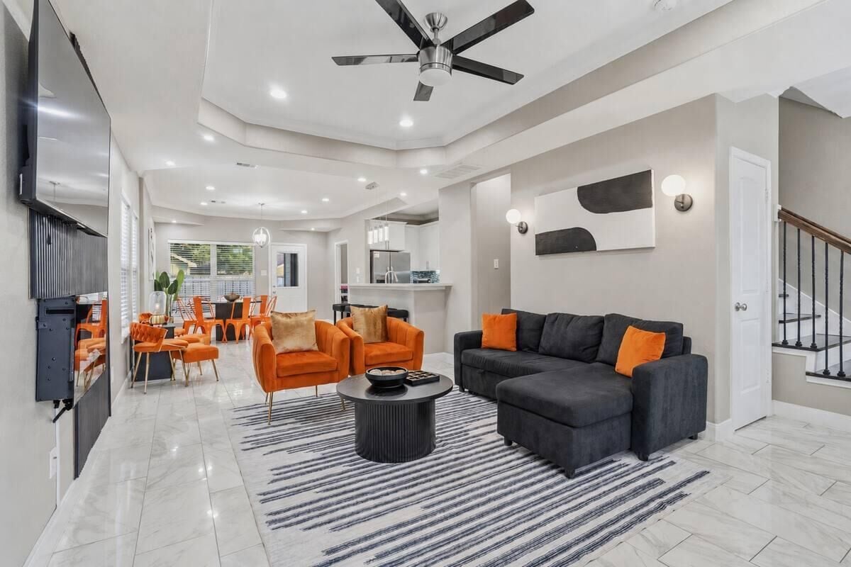 Un salón amplio con un sofá negro, sillones naranjas y una mesa de centro.