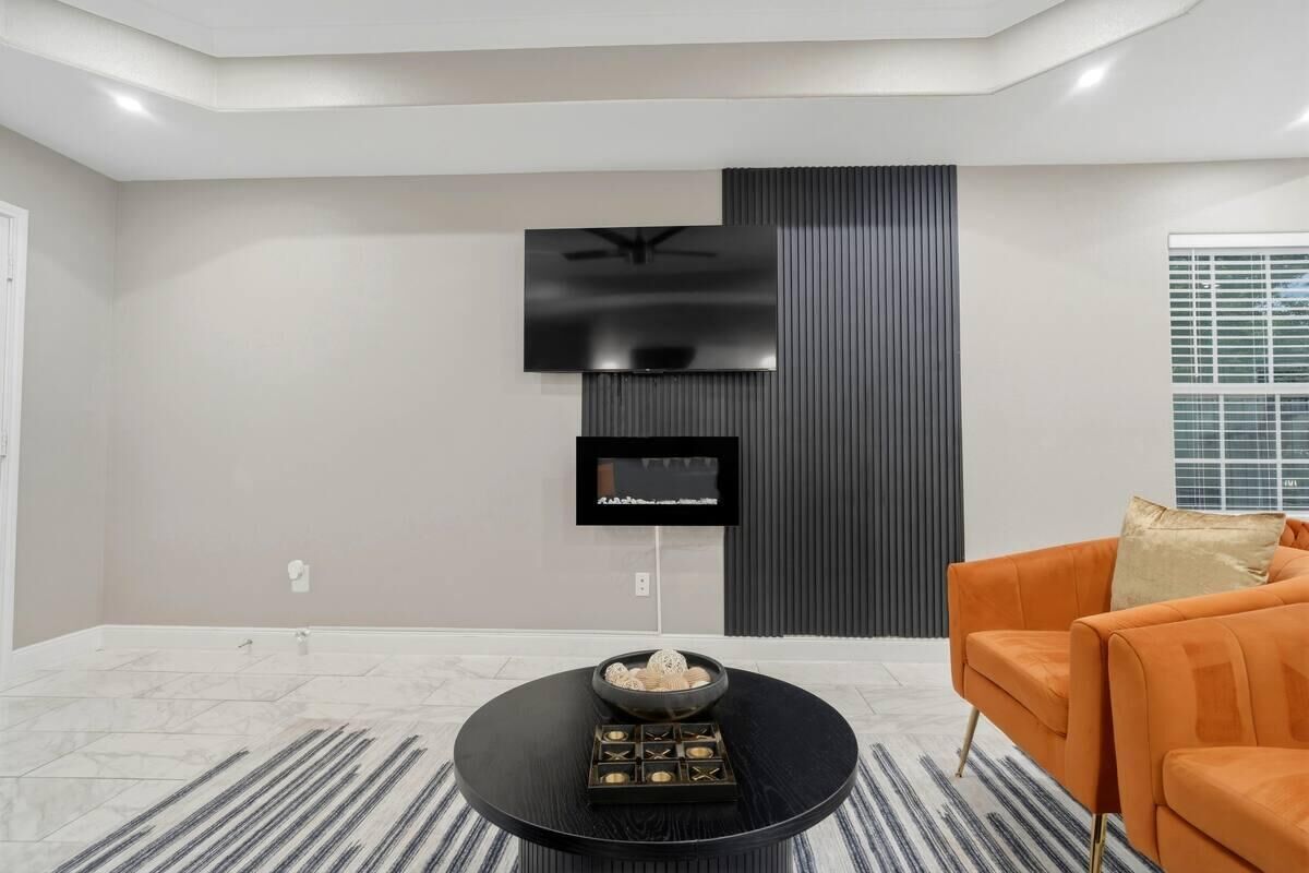 Un salon moderne avec un téléviseur à écran plat fixé au mur, une table basse ronde agrémentée d’objets décoratifs et un canapé orange.