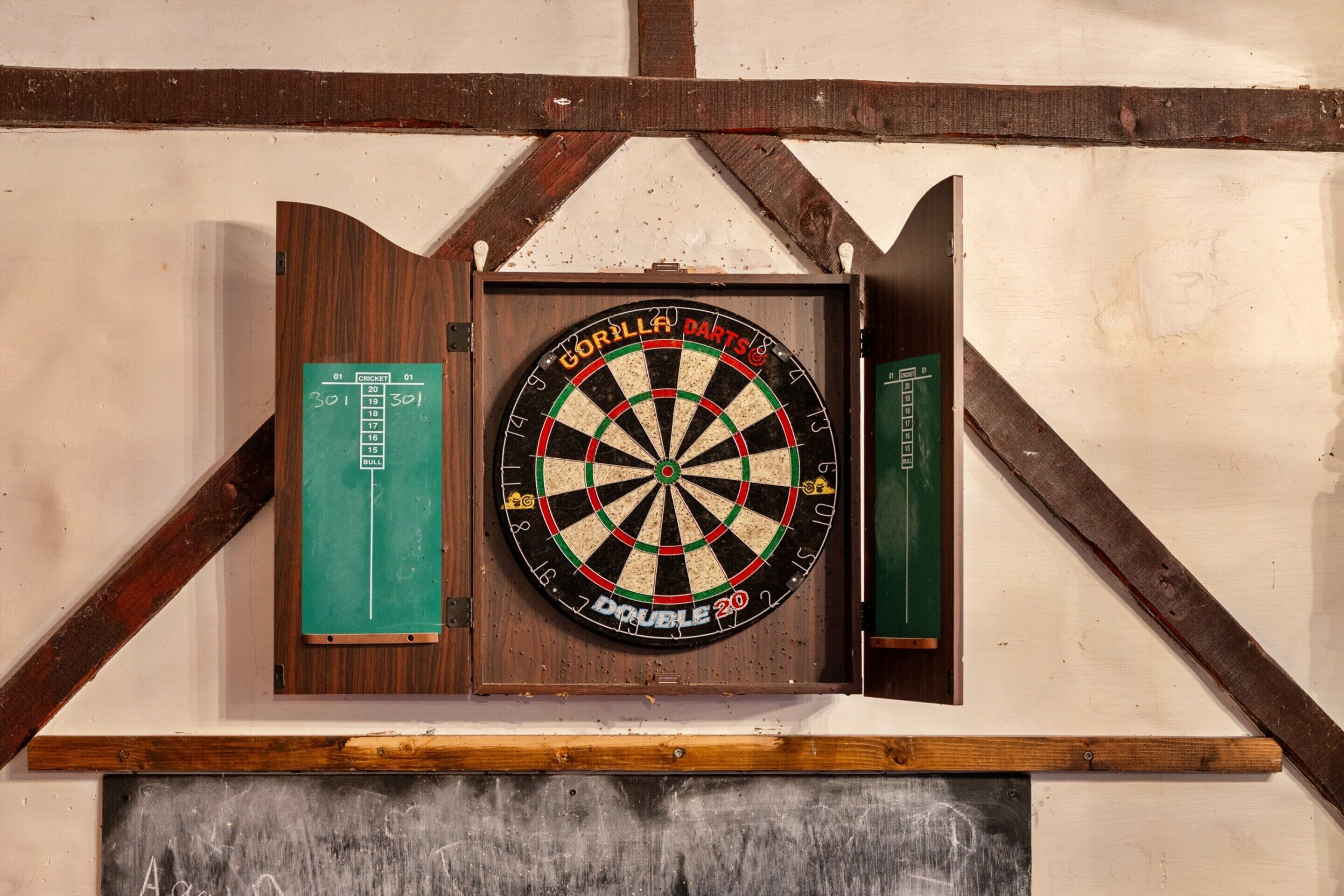 A dartboard mounted on a wall with a wooden frame and a chalkboard below.