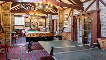 A billiards room with a pool table, a foosball table, and a ping pong table.