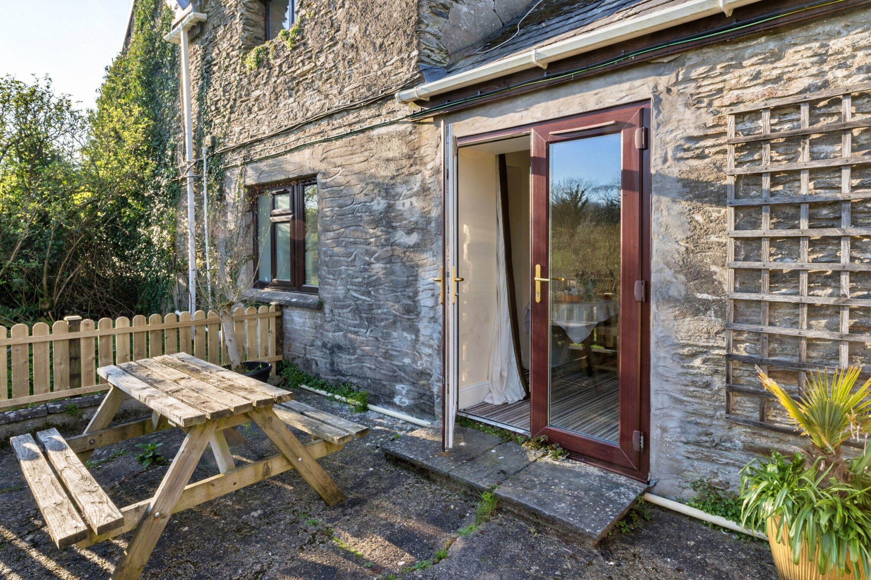 Un bâtiment en pierre avec une porte en bois et une fenêtre, un banc en bois et un petit espace aménagé en jardin.