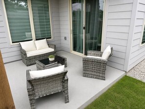 A patio with wicker furniture, including a sofa and two chairs, a small table with a plant, and a glass door leading to a covered area. - Luxe 3BR/3.5BA Garage. Patio. Near UTSW & DT (Dallas)