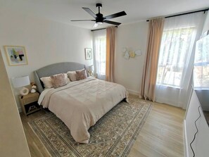 Ein Schlafzimmer mit Bett, Deckenventilator, Nachttisch, Teppich und Vorhängen.