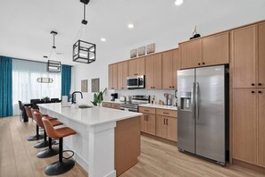 A modern kitchen with a central island, stainless steel appliances, and wooden cabinets. - Luxe 3BR/3.5BA Garage. Patio. Near UTSW & DT (Dallas)