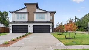 Uma casa residencial de dois andares com garagem, entrada por meio de rampa e um gramado bem cuidado.