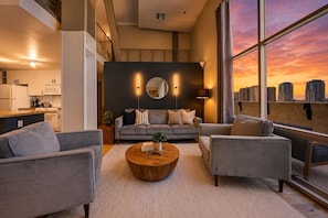 A modern living room with a city skyline view, a round wooden coffee table, and a grey sofa with striped pillows. - Explore Gaslamp from Chic Loft +Balcony City Views (San Diego)