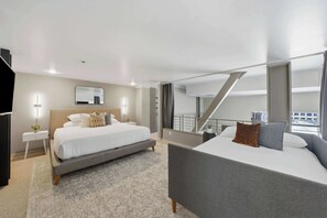 Una habitació d'hotel moderna amb un llit gran, un altre més petit, una taula de treball i una escala que condueix a un nivell superior.