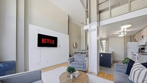 A modern living room with a mounted TV displaying 'NETFLIX,' a dining area with a round wooden coffee table, and a kitchen with white appliances. - Explore Gaslamp from Chic Loft +Balcony City Views (San Diego)