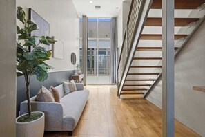 A modern interior with a grey sofa, a potted plant, and a staircase. - Explore Gaslamp from Chic Loft +Balcony City Views (San Diego)
