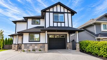 A two-story house with a black garage door, stone foundation, and a clear blue sky.